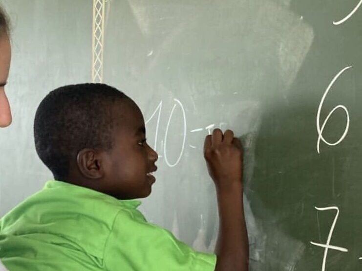 Una maestra volontaria della Missione Cuori Grandi regge in braccio un bambino di Amakpapé in Togo per permettergli di arrivare alla lavagna per completare un esercizio di matermatica