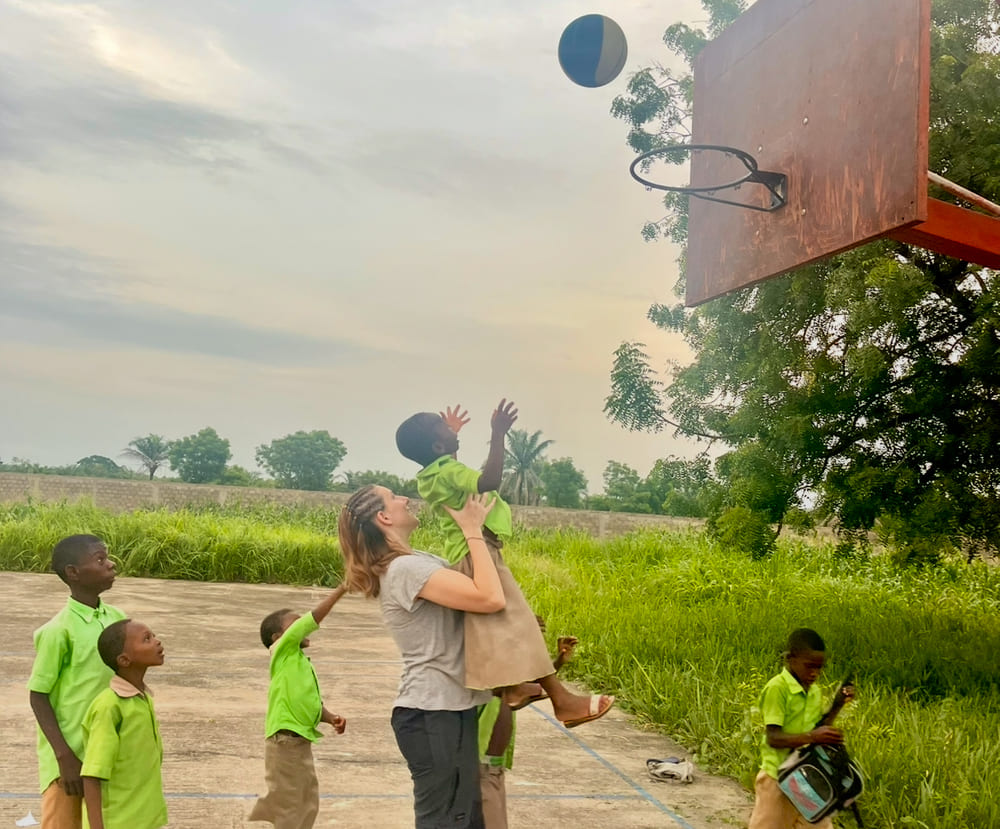 Una missionaria di Cuori Grandi fa fare canestro ad un bambino della scola materna prendendolo in braccio